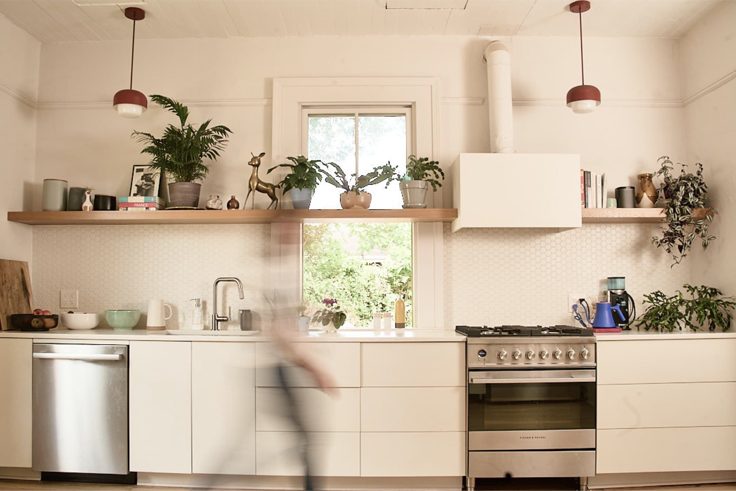 A kitchen by Basic Workshop with open shelves, plants, and a person passing through