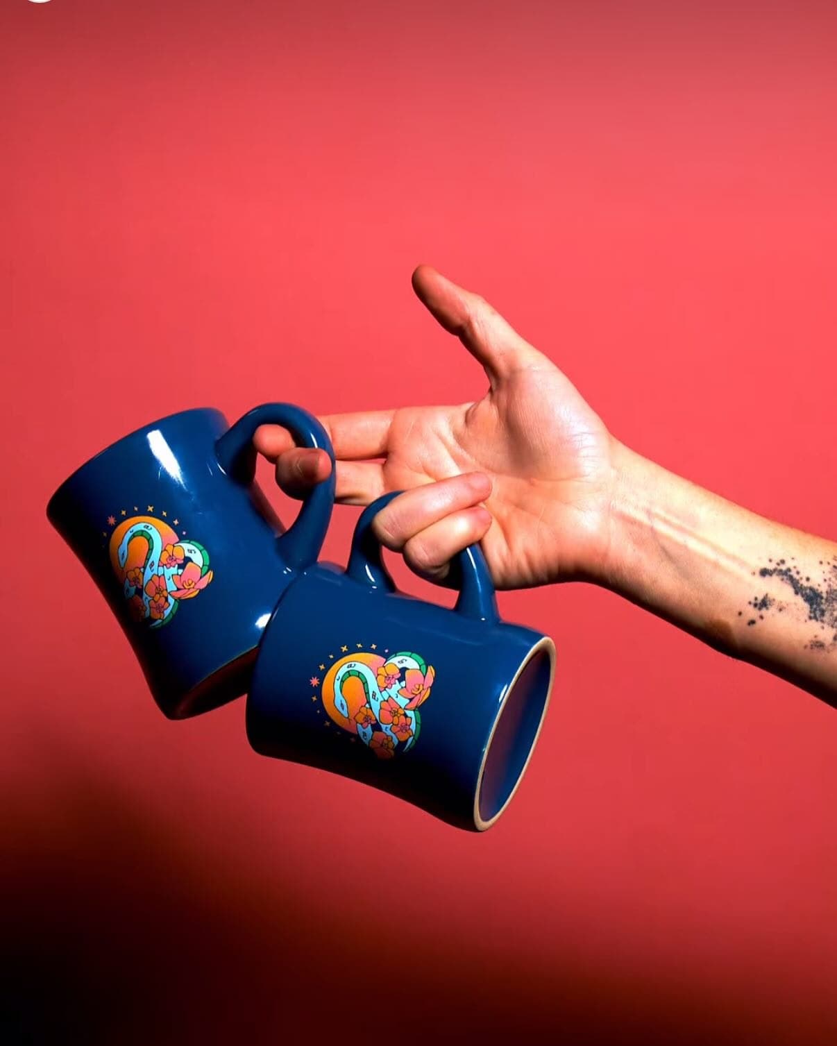A hand holding two blue snake mugs by their handles