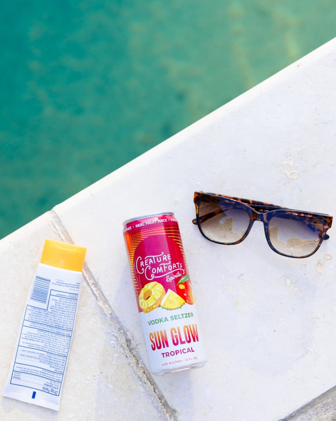 A can of Sun Glow poolside with sunglasses and sunscreen