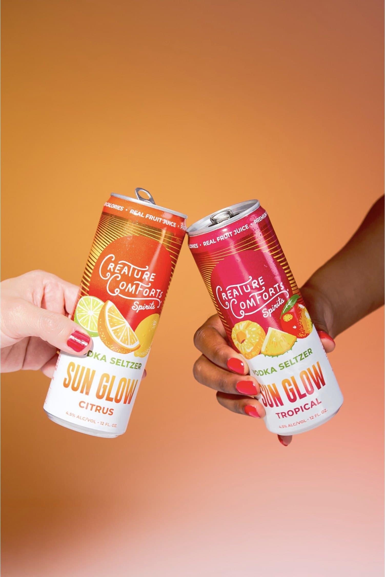Two hands toasting cans of Sun Glow Citrus and Tropical against an orange backdrop